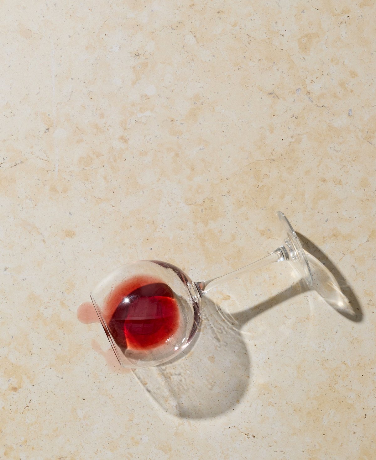 Fallen wine glass with red wine spilled across a light stone countertop surface
