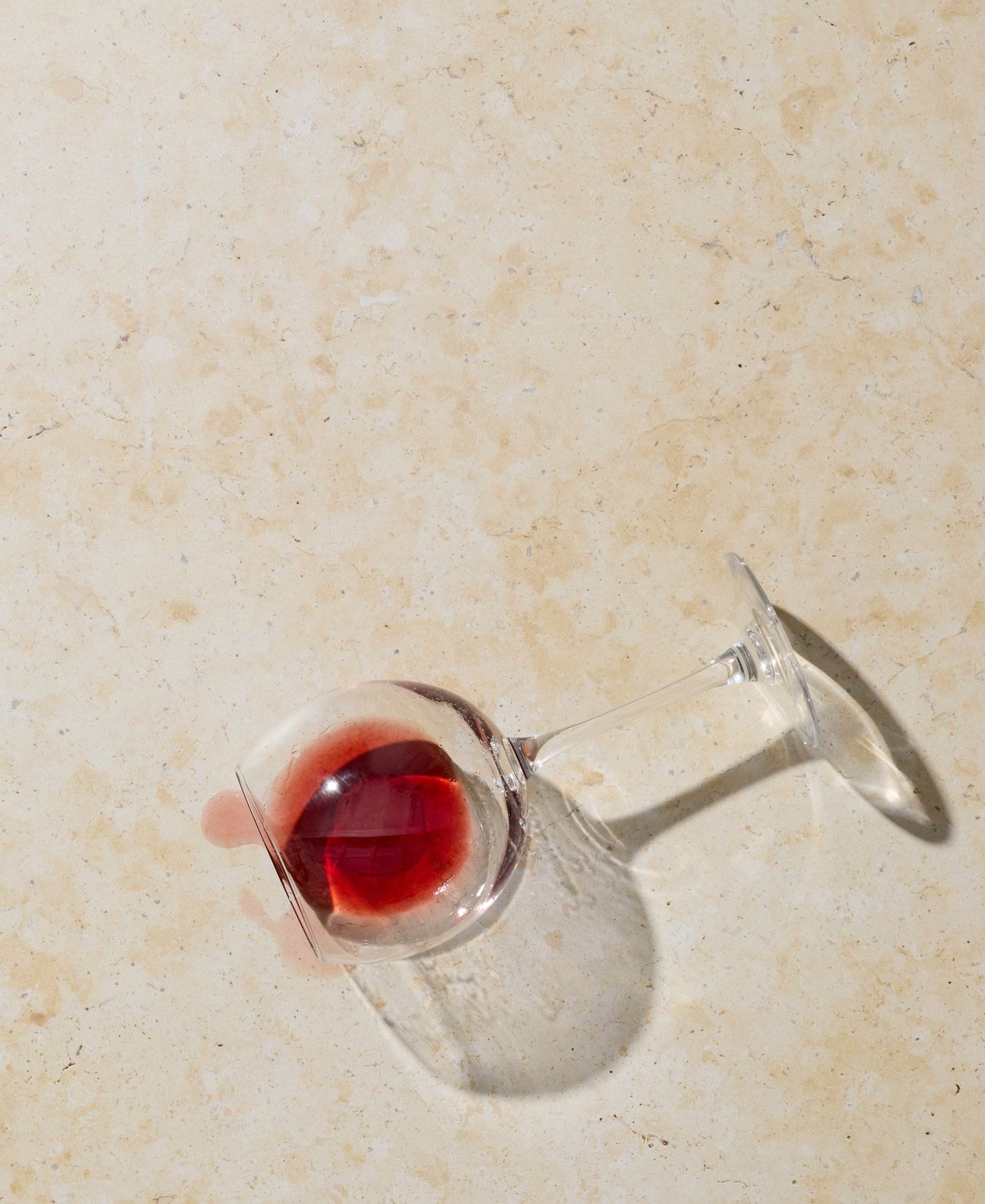 Fallen wine glass with red wine spilled across a white marble island surface