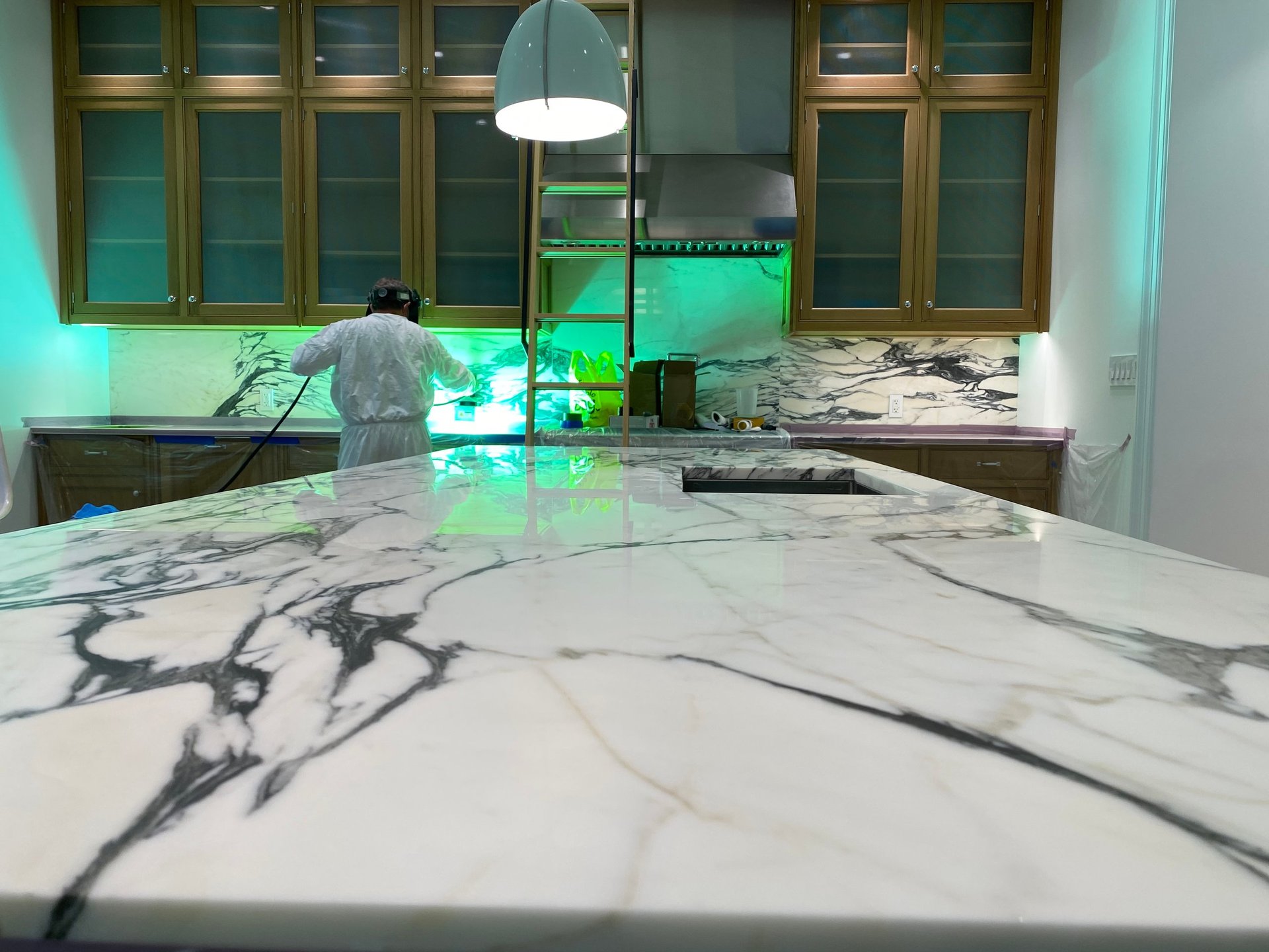 Modern kitchen with white marble countertops, wooden cabinetry, and green ambient lighting over the sink area
